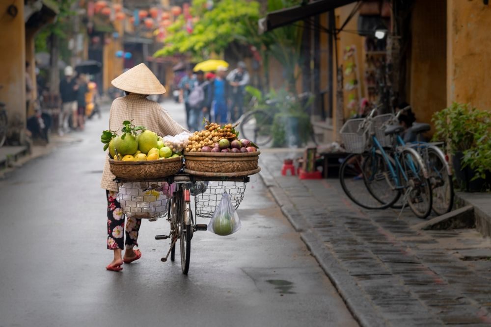 Kvinna med cykel och frukt på en gata i Vietnam