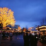 Besökare bland julbodar och upplysta träd på Liseberg i skymningen.