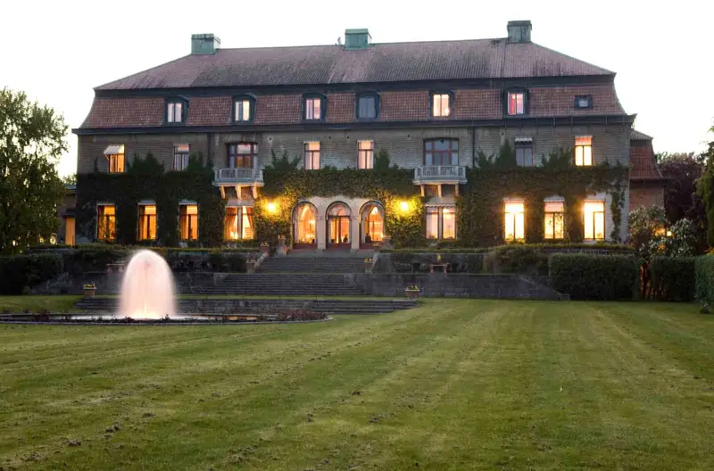Bjertorp Slott i kvällsljus med fontän och slottspark framför byggnaden.
