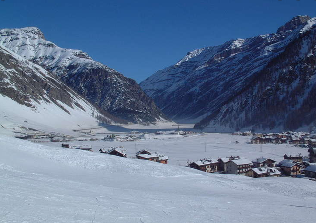 Snötäckt dalgång i Livigno med alpstugor och höga berg under blå himmel.