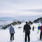 Skidåkare i en bred pist med snötäckta berg i bakgrunden.