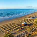 Utsikt över stranden i Playa del Inglés på Gran Canaria med Atlanten, palmer och sanddyner i bakgrunden
