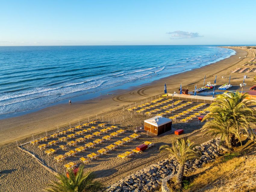 Utsikt över stranden i Playa del Inglés på Gran Canaria med Atlanten, palmer och sanddyner i bakgrunden