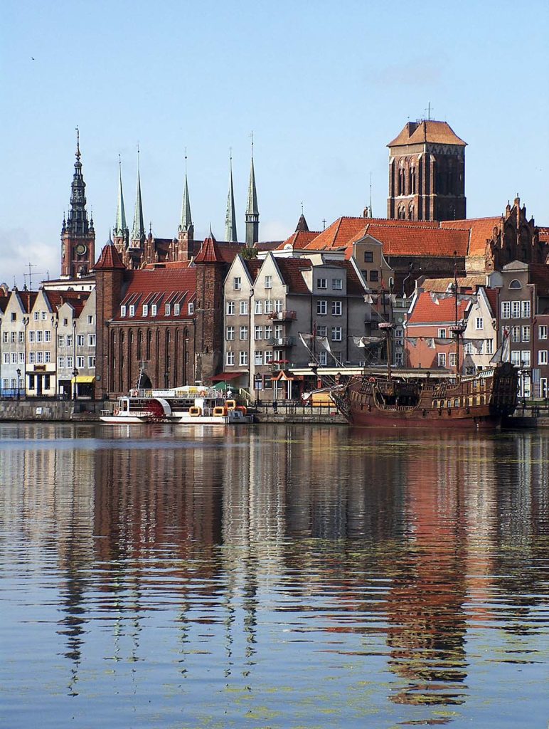 Vy över gamla stan i Gdansk vid floden Motława med historiska hus, kyrktorn och ett segelfartyg
