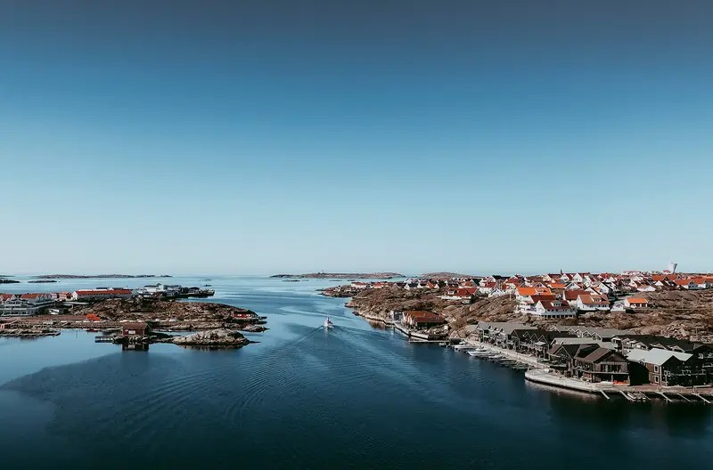 Vy över Smögen med sjöbodar, klippor och en båt på väg genom sundet.