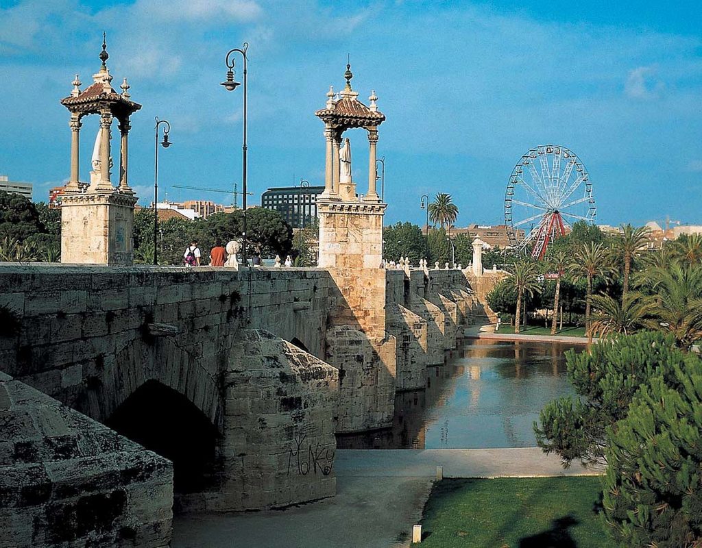 Stenbro över Turia-parken i Valencia med palmer, historiska torn och pariserhjul i bakgrunden
