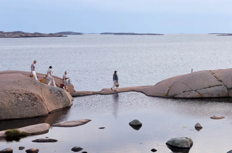 Strandflickornas Havshotell - Fyra personer promenerar över rundade granitklippor vid havet i Bohuslän.
