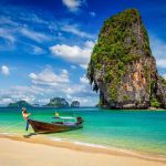 Longtailbåt vid strand och kalkstensklippa i södra Thailand