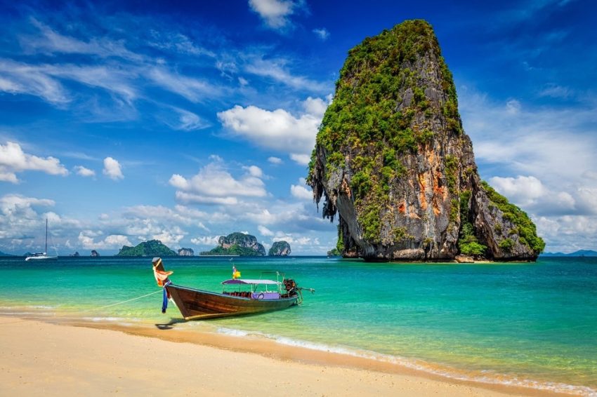 Longtailbåt vid strand och kalkstensklippa i södra Thailand
